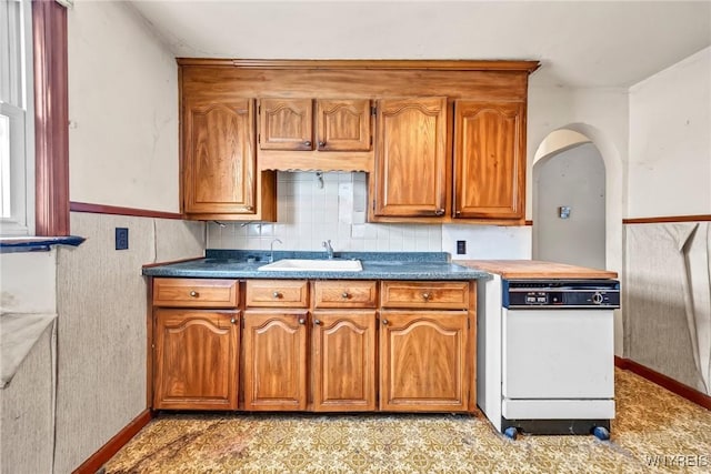 kitchen featuring arched walkways, brown cabinets, a sink, and dishwasher