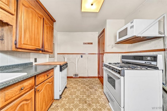 kitchen with white appliances, visible vents, backsplash, brown cabinets, and dark countertops