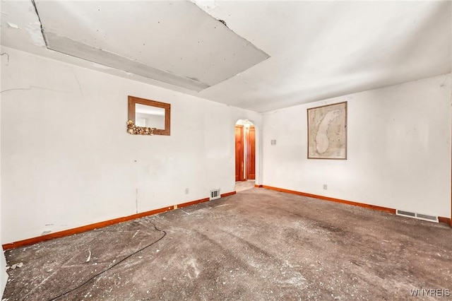 spare room featuring arched walkways, visible vents, and baseboards