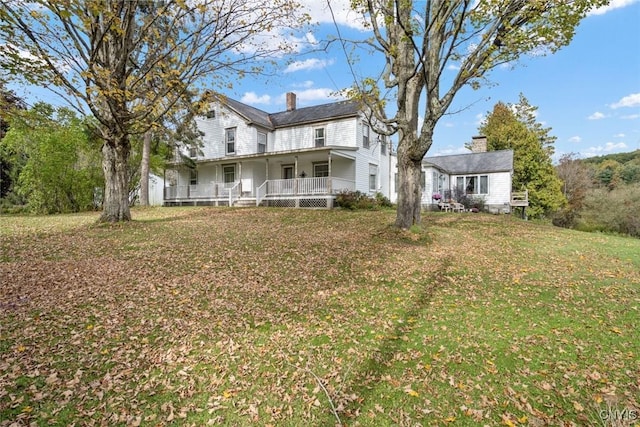 back of property featuring a chimney, a porch, and a yard