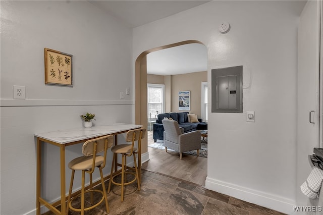 interior space featuring arched walkways, stone finish floor, electric panel, and baseboards