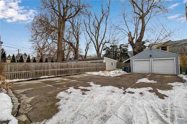 yard covered in snow with an outbuilding, a detached garage, and fence