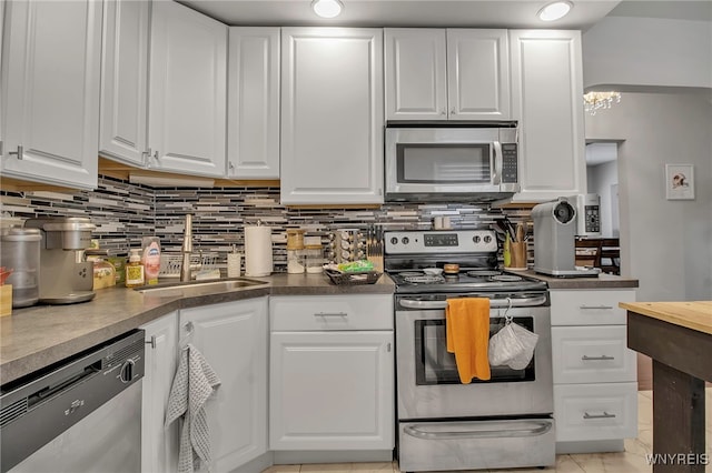 kitchen featuring stainless steel appliances, dark countertops, decorative backsplash, white cabinets, and a sink