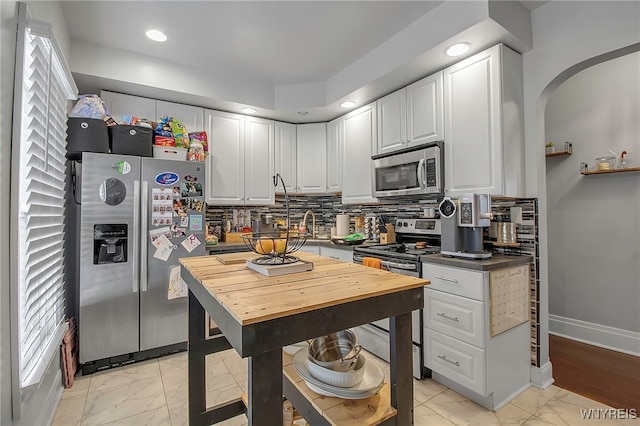 kitchen with tasteful backsplash, baseboards, white cabinets, appliances with stainless steel finishes, and marble finish floor