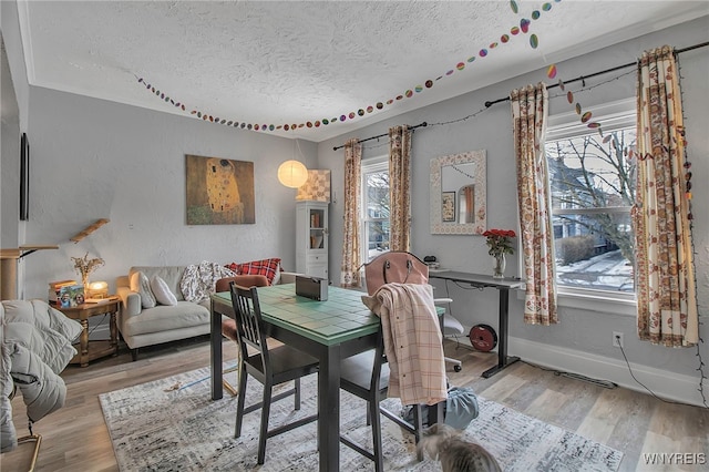 dining space featuring light wood finished floors, baseboards, a textured ceiling, and a textured wall