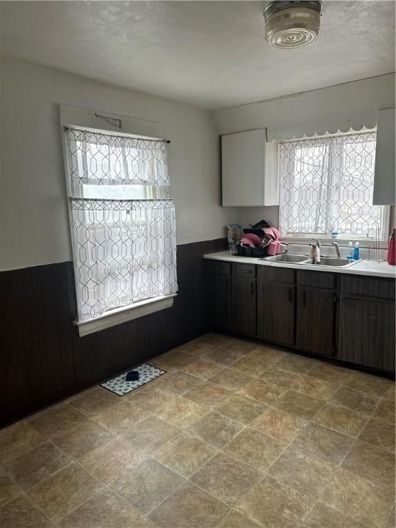 kitchen with a wainscoted wall, light countertops, a sink, and wood walls