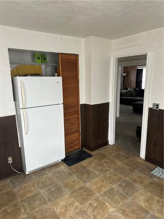 kitchen featuring a wainscoted wall, stone finish flooring, freestanding refrigerator, and wooden walls