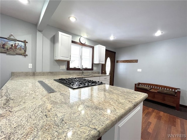 kitchen featuring dark wood-style floors, cooktop, white cabinetry, a sink, and a peninsula