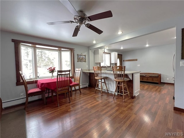 kitchen featuring a baseboard heating unit, a peninsula, a kitchen breakfast bar, light countertops, and dark wood-style floors