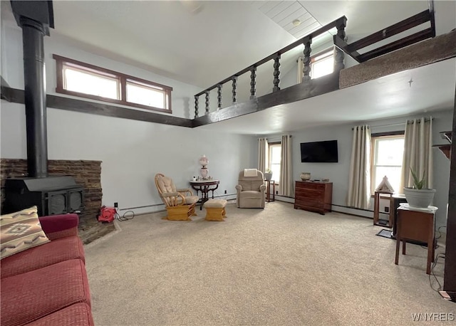 carpeted living room with a baseboard radiator, a wood stove, a healthy amount of sunlight, and a high ceiling