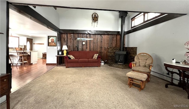 living area featuring a wood stove, wood walls, high vaulted ceiling, and carpet flooring