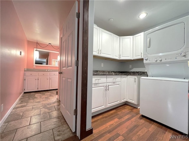 clothes washing area with a sink, baseboards, stacked washer / drying machine, cabinet space, and stone finish floor