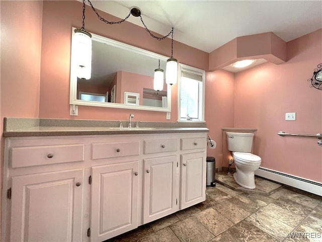 bathroom featuring toilet, a baseboard heating unit, stone finish floor, vanity, and baseboards