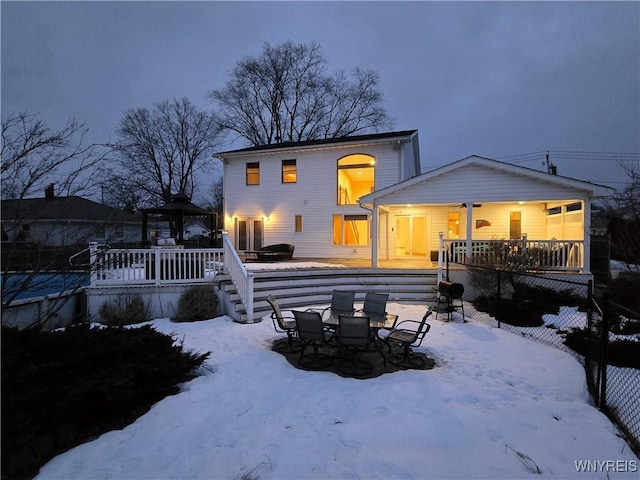 snow covered house with stairs, a gazebo, outdoor dining space, and a wooden deck