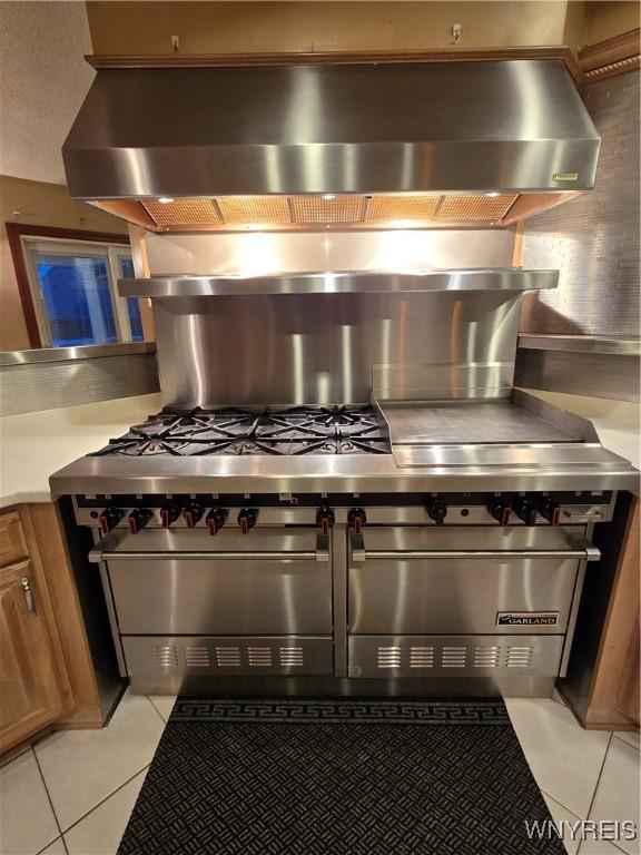 kitchen with light tile patterned floors, light countertops, double oven range, backsplash, and brown cabinets