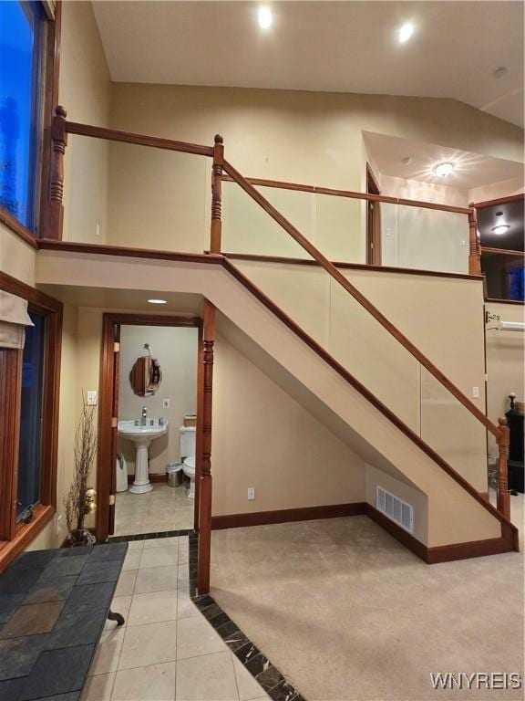 additional living space featuring light tile patterned floors, visible vents, a sink, high vaulted ceiling, and baseboards