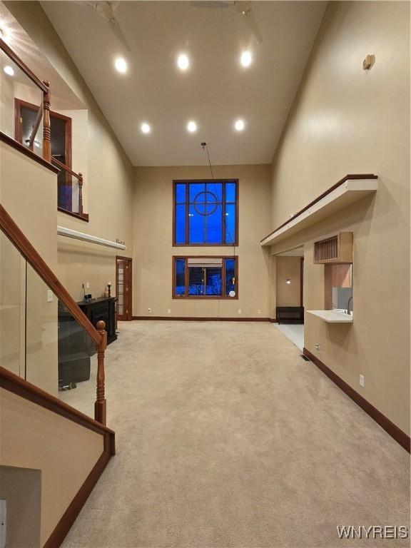 unfurnished living room featuring stairs, carpet flooring, a towering ceiling, and baseboards