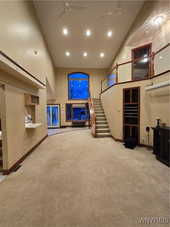 unfurnished living room with ceiling fan, a high ceiling, stairway, and carpet flooring