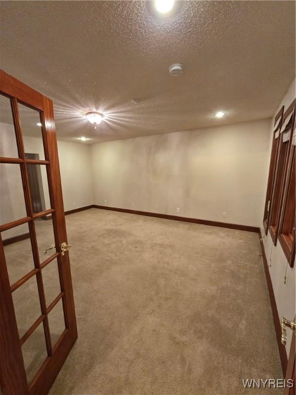 finished below grade area featuring a textured ceiling, french doors, carpet flooring, and baseboards