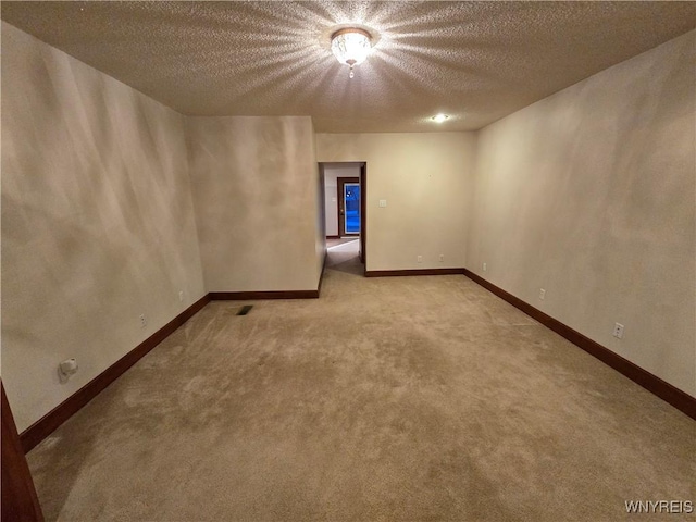 carpeted spare room featuring a textured ceiling and baseboards