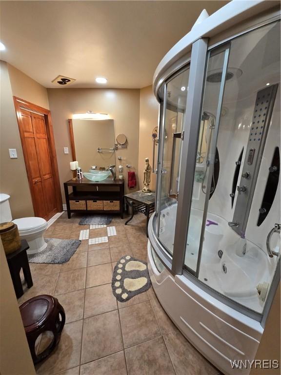 bathroom featuring toilet, a combined bath / shower with jetted tub, vanity, and tile patterned floors