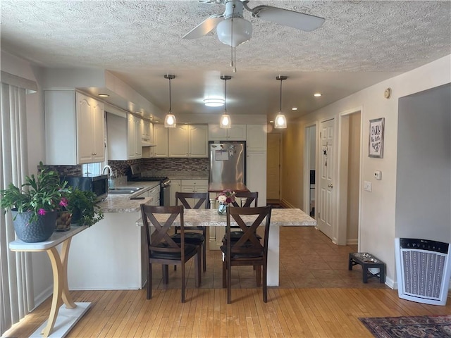 kitchen with a peninsula, a sink, appliances with stainless steel finishes, decorative backsplash, and light wood finished floors