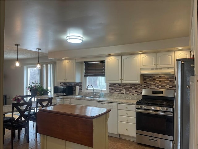 kitchen featuring light tile patterned flooring, under cabinet range hood, a sink, appliances with stainless steel finishes, and backsplash