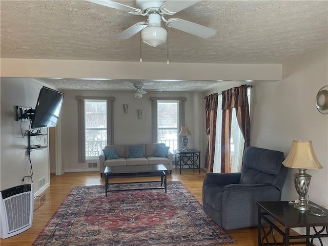 living area featuring visible vents, a textured ceiling, light wood-style flooring, and baseboards