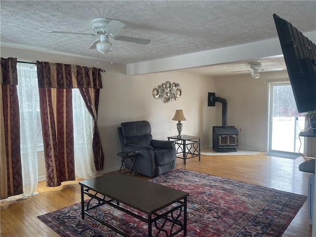 living room featuring a wood stove, ceiling fan, a textured ceiling, and hardwood / wood-style floors