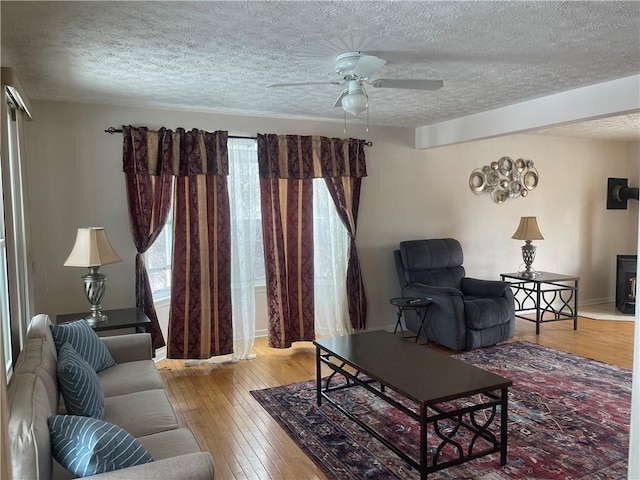 living area featuring ceiling fan, hardwood / wood-style flooring, a textured ceiling, and a wood stove