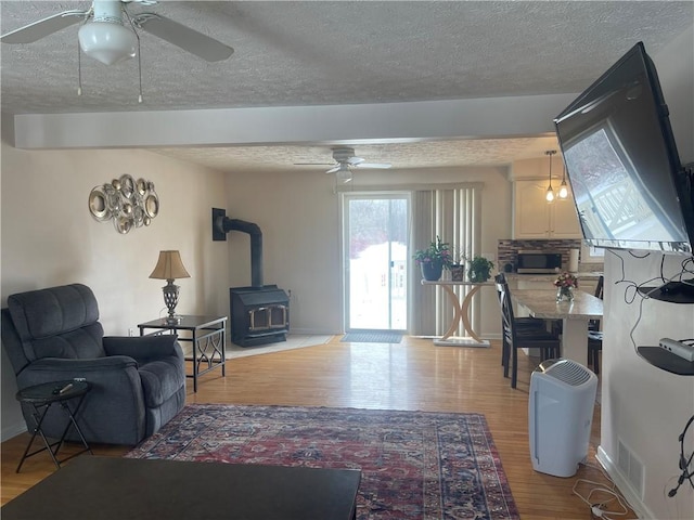 living area with a wood stove, a textured ceiling, a ceiling fan, and wood finished floors