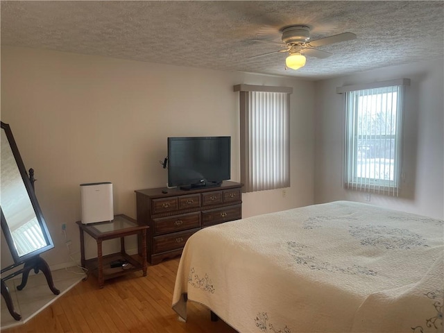 bedroom featuring light wood-style floors, ceiling fan, baseboards, and a textured ceiling