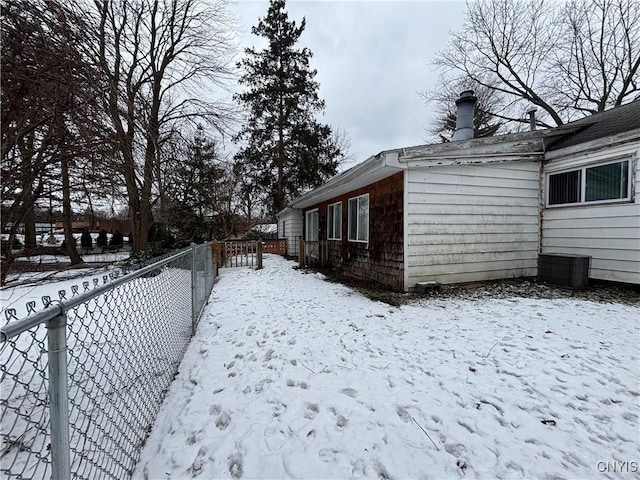 view of snowy exterior with fence and central AC