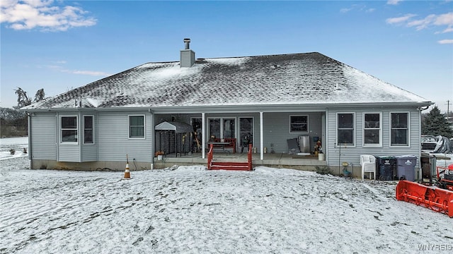 snow covered rear of property with a chimney and a shingled roof