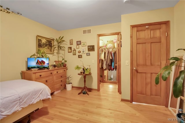 bedroom with visible vents, baseboards, light wood-style floors, and a walk in closet