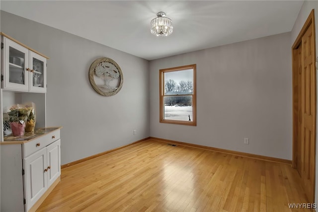 interior space featuring light wood finished floors, visible vents, an inviting chandelier, and baseboards