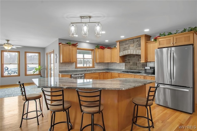 kitchen with light wood finished floors, decorative backsplash, appliances with stainless steel finishes, and a sink