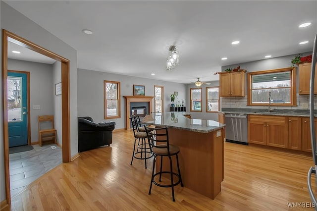 kitchen featuring tasteful backsplash, light wood-type flooring, a kitchen bar, stainless steel dishwasher, and a sink