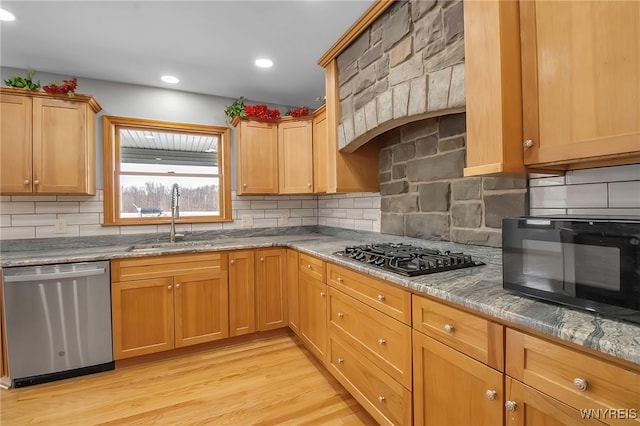 kitchen featuring backsplash, light stone countertops, light wood-type flooring, black appliances, and a sink