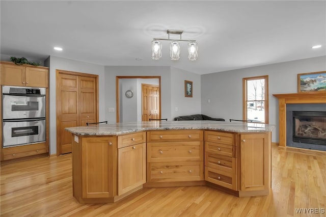 kitchen featuring stainless steel double oven, a glass covered fireplace, open floor plan, and light wood finished floors