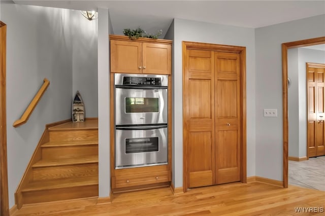 kitchen with stainless steel double oven, baseboards, and light wood-style floors