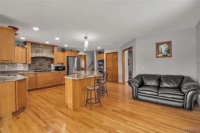 kitchen with a breakfast bar, open floor plan, appliances with stainless steel finishes, and light wood-type flooring