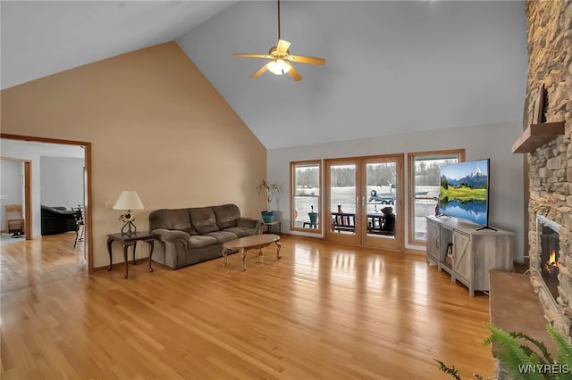 living area featuring light wood finished floors, a fireplace, french doors, high vaulted ceiling, and a ceiling fan