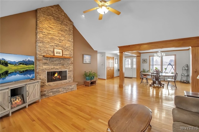 living room featuring a stone fireplace, ceiling fan with notable chandelier, high vaulted ceiling, and light wood-style floors