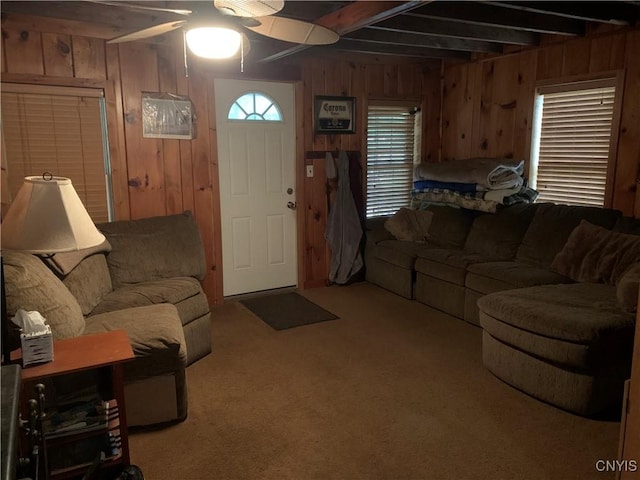 carpeted living area with a ceiling fan, wood walls, and beamed ceiling