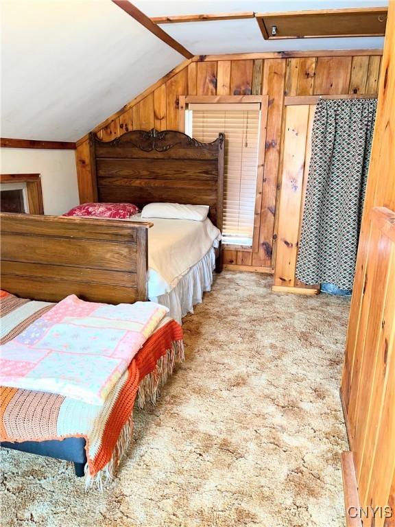 carpeted bedroom with lofted ceiling and wooden walls