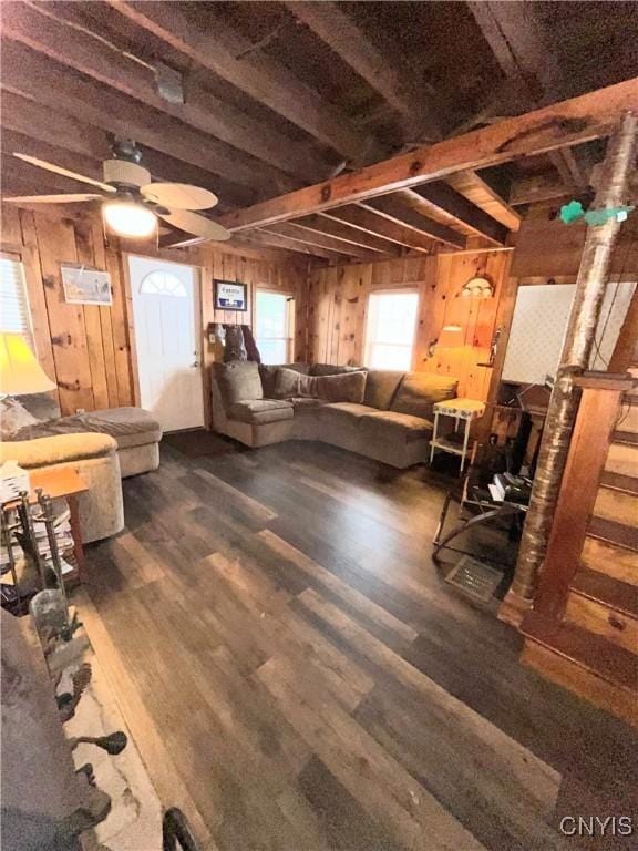 unfurnished living room featuring ceiling fan, wooden walls, beam ceiling, and dark wood-style flooring