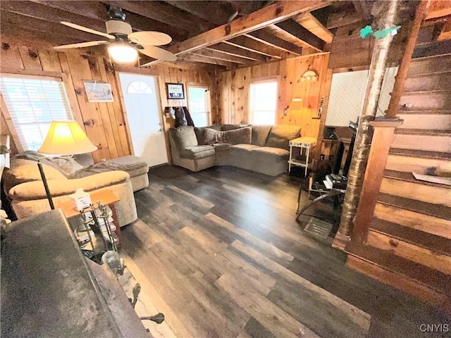 living area featuring a ceiling fan, wood walls, wood finished floors, beamed ceiling, and stairs