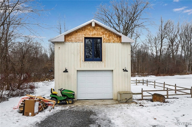 snow covered garage with a detached garage and fence