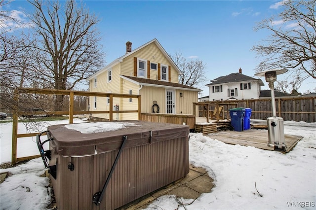 snow covered property with a chimney, fence, a wooden deck, and a hot tub